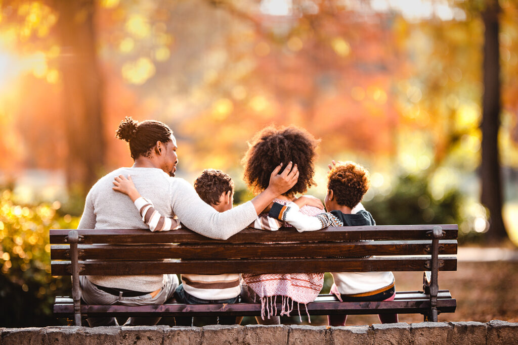 Rear view of African American family embracing while relaxing on a park bench in autumn day.