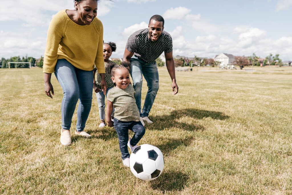 Family with kids playing soccer in soccer field